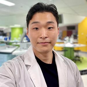 A portrait shot of CUA graduate Kenny Paek wearing a science lab coat