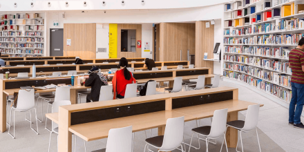 A wide angle shot of CUA Library showing rows of books with different colours and students studying