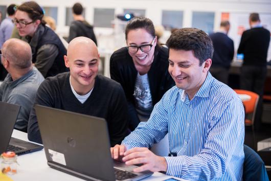 3 smiling people look at a laptop screen 