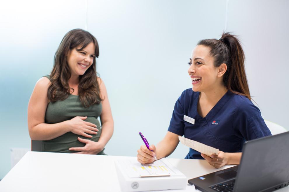 a smiling nurse in front of a laptop with a smiling pregnant woman