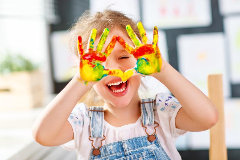 Child laughing, showing hands covered with paint